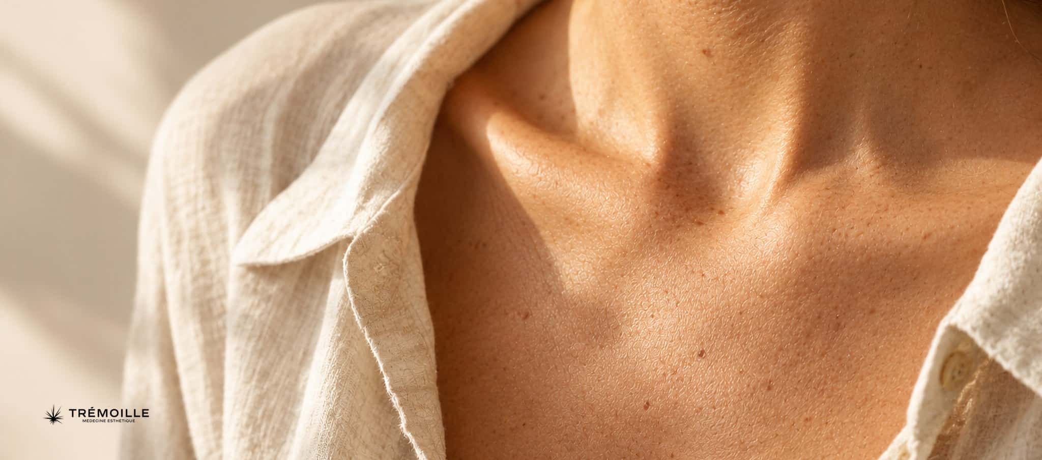 Gros plan photographique sur la peau du décolleté et de la clavicule, lumière douce d’été, sans visage
